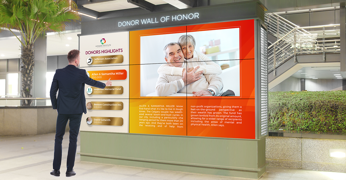 A man standing in front of a donor wall focusing on donor highlights.